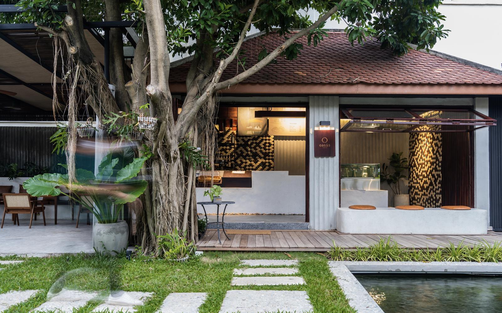Oasis Café: a tiled-roof café under a large old tree, with a garden, stepping stones and a pond in front